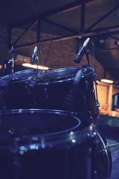 Drum kit with microphones under warm venue lights on dark stage Stock Photos