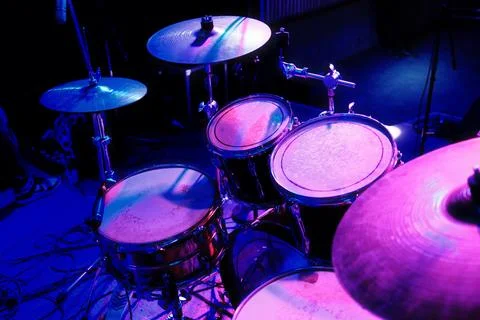 Drum set on stage bathed in vibrant blue and purple light Stock Photos
