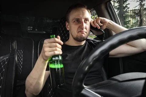 Drunk aggressive driver with a bottle of Alcohol driving a car, talk on the Stock Photos