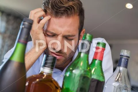 Drunk businessman slumped beside many spirit bottles Stock Photos