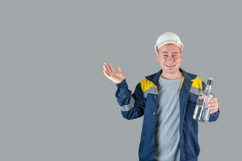 Drunk construction worker in work clothes and hardhat holds a bottle of alcoh Stock Photos