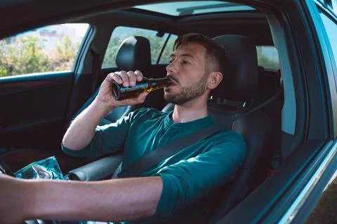 Drunk driver. Young man drinking beer while driving a car Stock Photos