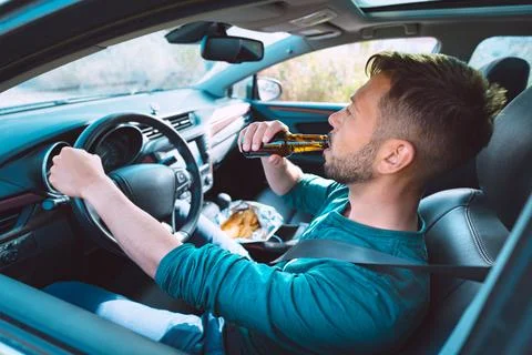 Drunk driving. Young man drinking beer while driving a car Stock Photos