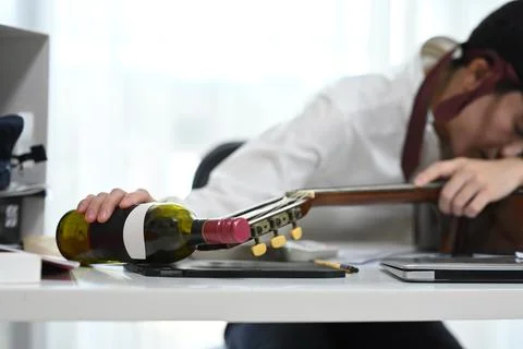 Drunk employee sleeping on desk with a bottle of wine and a guitar Stock Photos