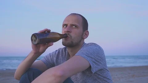 Drunk man drinking beer on the sea beach in the evening. Portrait of a man Видео 108493660