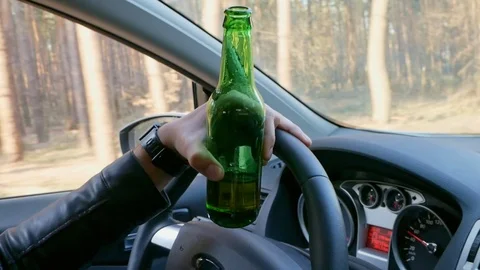 Drunk man driving car with a bottle of beer in his hand in close up Stock Footage 106684164
