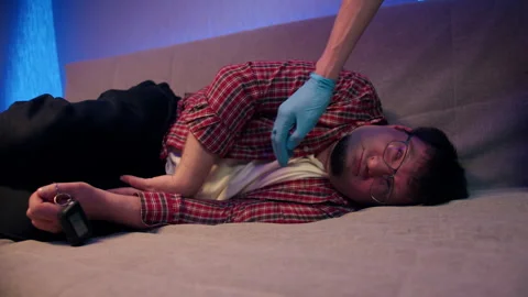 Drunk man lies on sofa while blue gloved caregiver reaches for urgent care Stock Footage 340096285