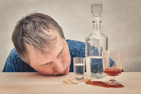 The drunk man put his head on the table in front of a bottle of alcohol. Stock Photos