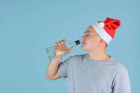 A drunk man in a red Santa hat drinks strong alcohol from the throat of a bot Stock Photos