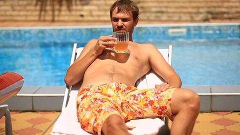 A drunk man in shorts drinking beer by the pool Stock Footage 77195509