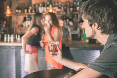 Drunk man sitting at bar, drinking cocktail, looking at girls Stock Photos