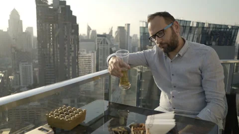 Drunk man sitting in skybar and drinking beer Stock Footage 90554283