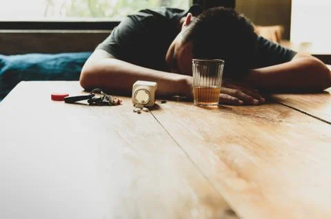 Drunk man sleeping on table with pills and glass of whiskey and car keys. Stock Photos