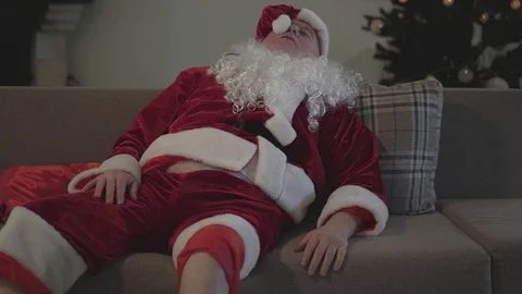 Drunk old man with false white beard in the costume of Santa Claus lying on the Stock Footage 120911793