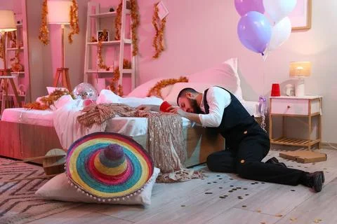 Drunk young man with cup sleeping after party in bedroom Stock Photos