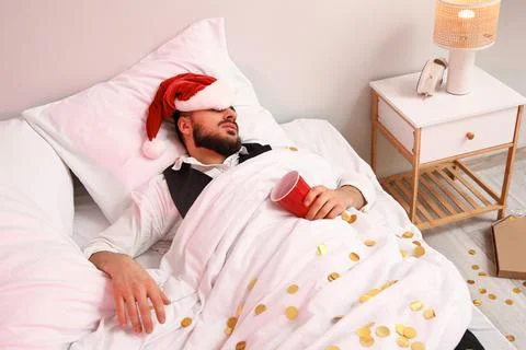 Drunk young man with Santa hat sleeping after Christmas party in bedroom Stock Photos
