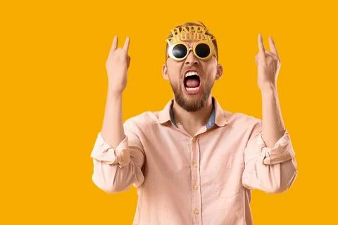 Drunk young man showing "devil horns" after Birthday party on yellow backgrou Stock Photos