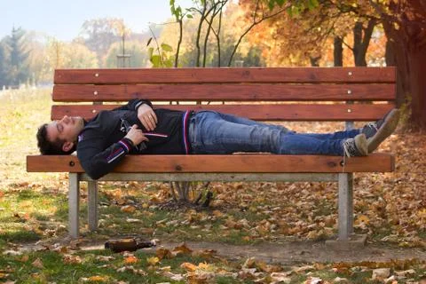 A drunk young man sleeping on a bench in the day. Stock Photos