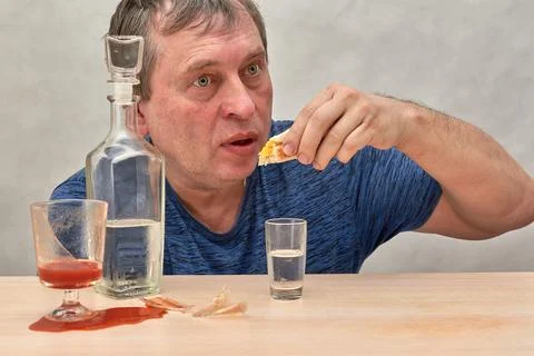 A drunkard sitting at a table seizes alcohol alone. Stock Photos