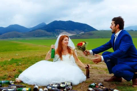 Drunken bride with lots of empty beer bottles in mountain landscape  and groom Stock Photos
