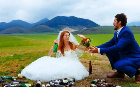 Drunken bride with lots of empty beer bottles in mountain landscape  and groom Foto stock