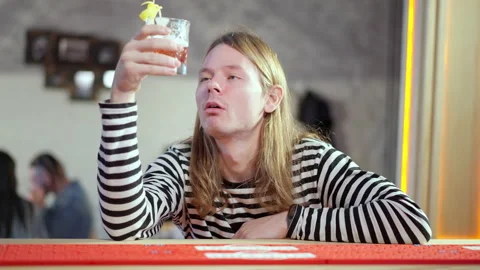 Drunken frustrated young man sitting at bar counter holding glass with drink and Stock Footage 149788079