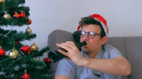 Drunken guy in red cap nerd drinking wine from bottle at Christmas holidays. Video stock 136055253