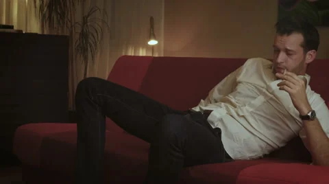 Drunken young playboy wakes up on the couch, smokes cigarette and drinks whiskey 스톡 동영상 54640927