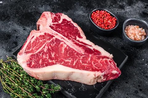 Dry-aged Raw T-bone or porterhouse beef meat Steak with herbs and salt. Black Stock Photos