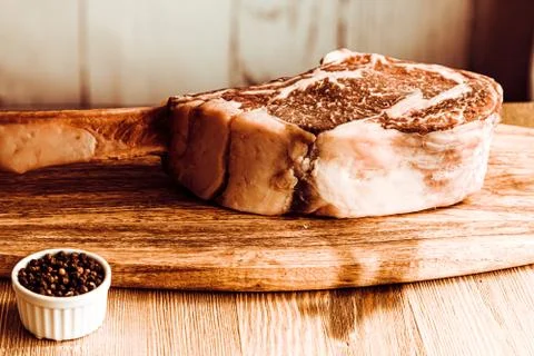 Dry aged raw tomahawk beef steak on wooden board and pepper Stock Photos