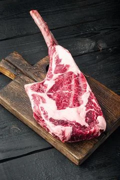 Dry aged raw tomahawk beef steak with ingredients for grilling, on black wood Stock Photos