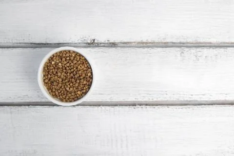 Dry buckwheat in white ceramic bowl isolated on grey table. Spilled buckwheat. Stock Photos