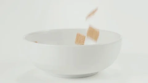 Dry cereal tumbles in slow motion into a bowl on a white cyc Stock Footage 70682642