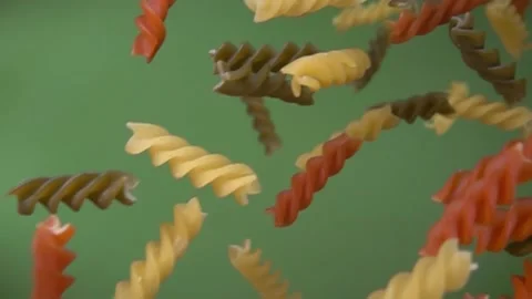 Dry colored pasta fusilli falling diagonally on the green background Stock Footage 233613680