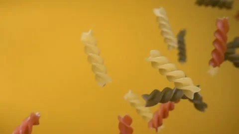 Dry colored pasta fusilli falling diagonally on yellow ochre background Stock Footage 233844366