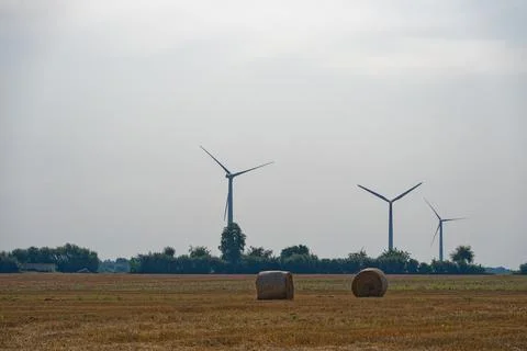 Dry cut field with two hay bales and distant wind turbines behind. Stock Photos