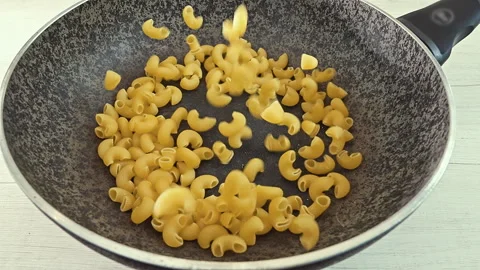 Dry Elbow Macaroni Pasta Falling into a Black Cooking Pot Vídeos de archivo 344985325