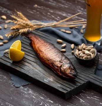 Dry fish served with lemon, on dark wood board with pistachio, beer Stock Photos
