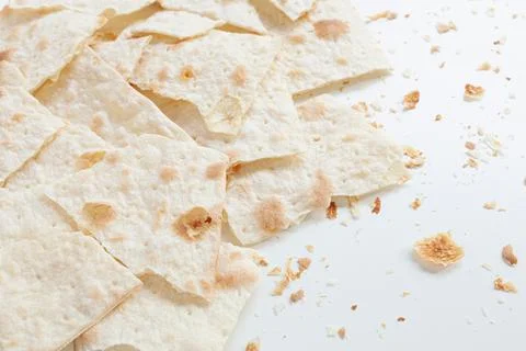 Dry flat bread broken in pieces and divided, with crumbs, on white background Stock Photos