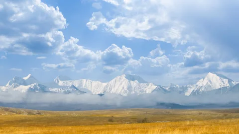 Dry grass prairie before mountain chains in a snow under a cloudy sky Stock Footage 146688803