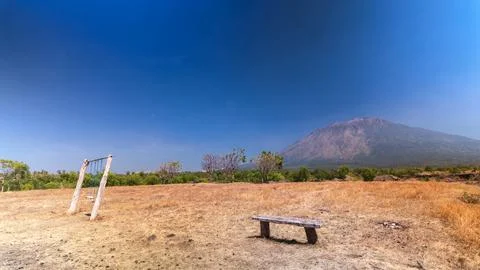 Dry grassy landscape with a rustic bench, swing set, and a large mountain Stock Photos