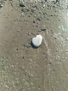 Dry light gray rounded stone in the shape of a heart lies on the wet sand Foto stock