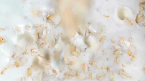 Dry oatmeal flakes fall into white yogurt or milk Video stock 332281257