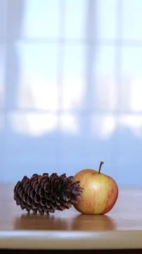 A dry pine cone and a small red-yellow apple lie side by side on a wooden table Stock Photos