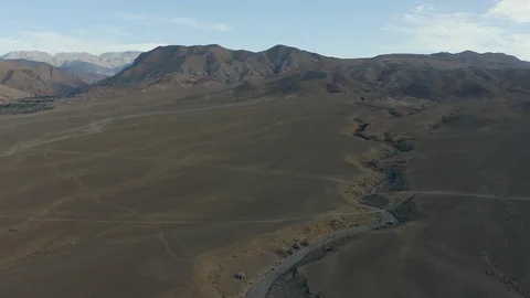A dry river scars a desert plain, a jagged ridge of mountains on the horizon. Stock Footage 127014069