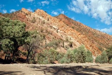 Dry riverbed with red hill of vertically layered rock Stock Photos