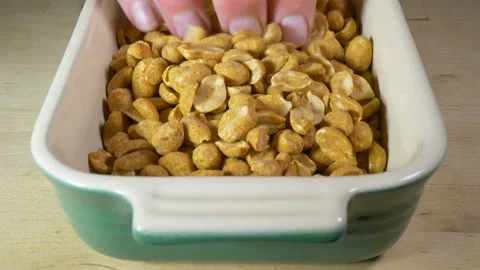 Dry roasted peanuts pouring into a dish, then a hand taking some. Stock Footage 145831574