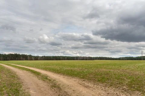 A dry sandy road passes through a field under the scorching sun and clouds. D Фото