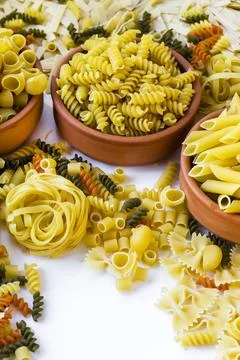 Dry various types of pasta in ceramic casserole on white surface Stock Photos