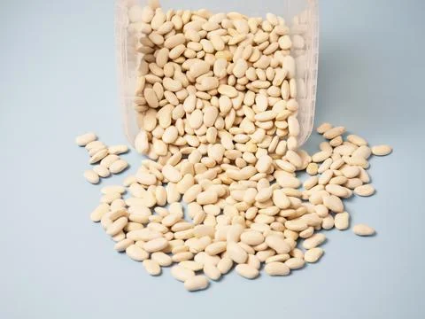 Dry white beans scattered from a plastic container on a blue table. copy spac Stock Photos